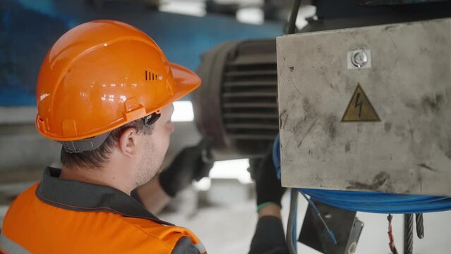 Industrial engineer inspects and maintains heavy machinery, electrical motor. Expertise and safety measures in a factory workshop. Worker in helmet
