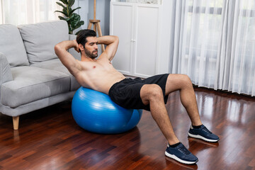 Athletic and sporty man doing situp on fitness ball during home body workout exercise session for...
