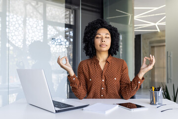 A serene businesswoman meditating at her workspace, surrounded by natural light and modern office...