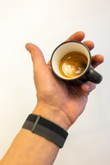 Hand holding a freshly brewed espresso in a black cup