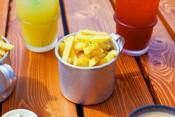 French fries in metal cup and lemonades on brown boards wooden table. Fast food, potato. Outdoor...