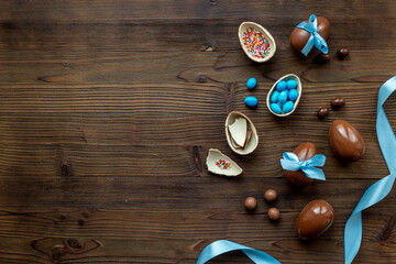 Chocolate Easter eggs in blue ribbon with sweets on brown wooden background
