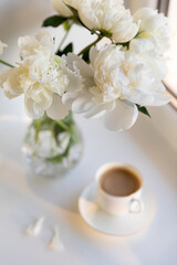 Peonies and Morning Coffee on a Table. A serene scene featuring a bouquet of lush white peonies beside a delicate cup of coffee with soft natural light. Calm and cozy ambiance. Focus on flowers.