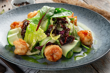 Salad with grilled shrimp and fresh green vegetables, spinach leaves and zucchini in blue plate. Healthy seafood salad with pesto sauce, close up - Powered by Adobe