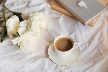 An inviting scene of a warm coffee cup and lush peonies on a bed, capturing the vibe of a relaxed...