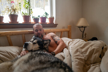 Man cuddling  Alaskan malamute dog in bed in the morning