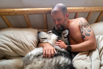 Man cuddling  Alaskan malamute dog in bed in the morning