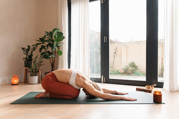 Calm, peaceful caucasian blond woman is practicing balasana child's yoga pose at home indoors,...