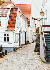 Charming historic old town street in Bergen with traditional white wooden houses and red-tiled roofs . Norway