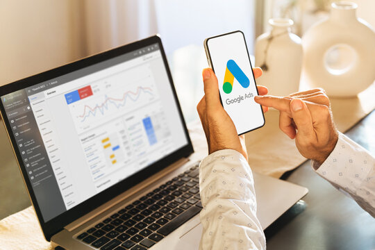 Man using a mobile phone with Google Ads on the screen and in the background a computer showing ad statistics. Rosario, Argentina - March 23, 2024