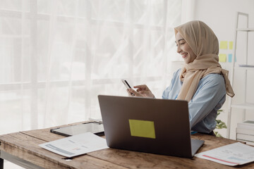 Muslim female economist working online with accounting documents on modern laptop device, writing,...