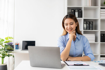 Beautiful Asian female accountant smiling while working with laptop and documents about finance,...