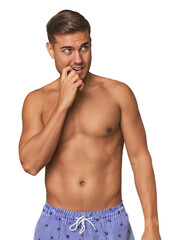 Fototapeta premium Young man shirtless in swimwear, studio relaxed thinking about something looking at a copy space.