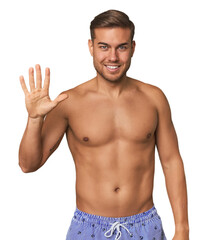 Fototapeta premium Young man shirtless in swimwear, studio smiling cheerful showing number five with fingers.