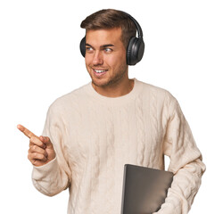 Young student man with a laptop smiling and pointing aside, showing something at blank space.