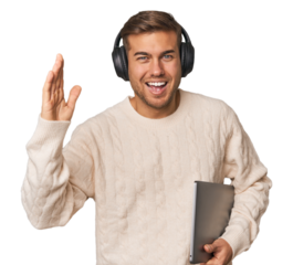 Young student man with a laptop receiving a pleasant surprise, excited and raising hands.