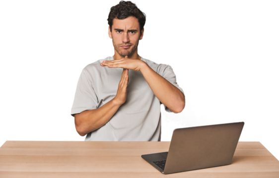 Hispanic young man working on laptop showing a timeout gesture.