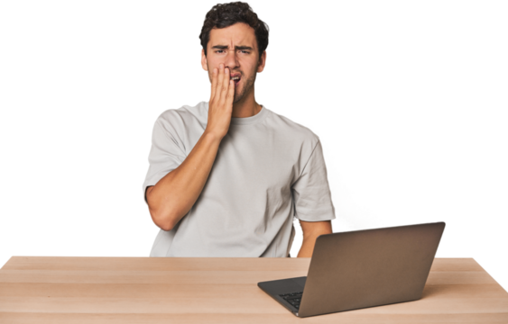 Hispanic young man working on laptop yawning showing a tired gesture covering mouth with hand.