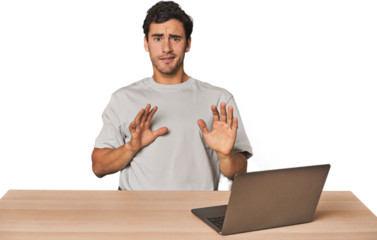 Hispanic young man working on laptop rejecting someone showing a gesture of disgust.