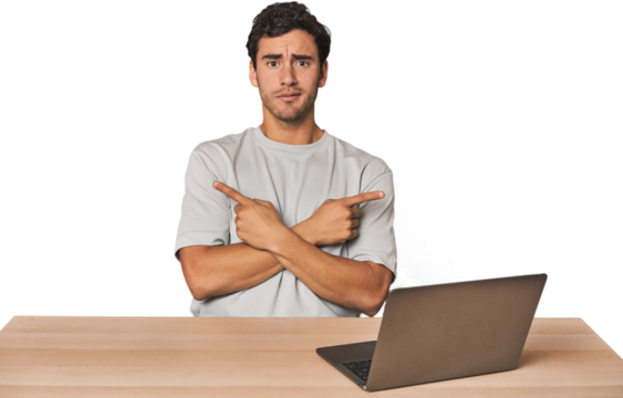 Hispanic young man working on laptop points sideways, is trying to choose between two options.