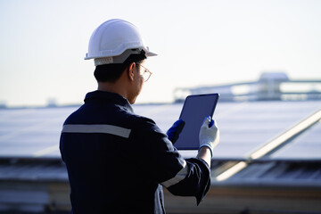 A man wearing a hard hat and safety glasses is looking at a tablet. He is likely a worker in a...