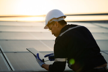 A man wearing a hard hat and safety glasses is using a tablet to look at a solar panel