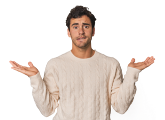 Young Hispanic man in studio confused and doubtful shrugging shoulders to hold a copy space.