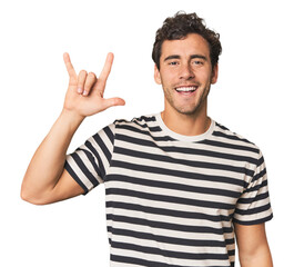 Young Hispanic man in studio showing a horns gesture as a revolution concept.