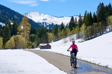 smiling senior woman riding her electric mountain bike on a sunny day in early spring in the...