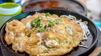 On a hot, black pan, a pan fried oyster omelet with bean sprouts. In the hot pan, this menu is ready to be served and consumed.