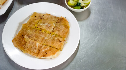 chicken Mataba on a white plate and a bowl of dipping sauce next to it. All This Menu is on stainless surface table.