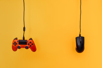 A red gamepad and a computer mouse hang on wires against a yellow background.