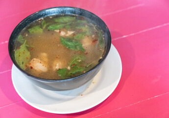 Traditional thai spicy Tom yum soup with chicken served in black bowl and on white dish with wooden pink table