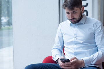 portrait d'un beau jeune homme assis au bureau qui utilise son téléphone portable pour communiquer