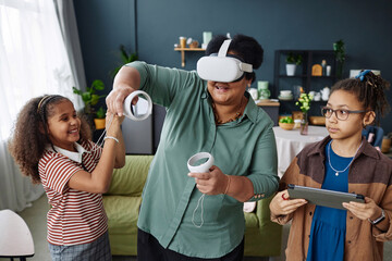 Waist up portrait of senior Black woman playing VR game with two little girls at home and having fun together
