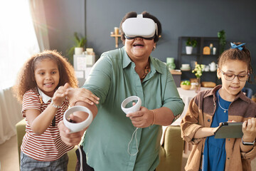 Waist up portrait of modern senior Black woman playing VR game with little girls in sunlight and having fun