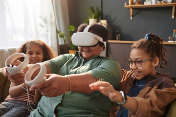 Portrait of happy Black grandmother with two little girls enjoying VR gaming at home together