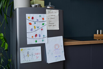 Close up background image of childrens drawings on refrigerator in modern kitchen interior, copy space