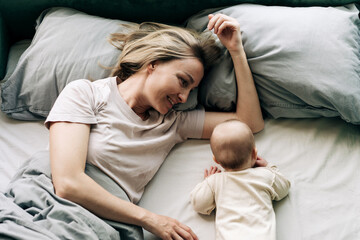 A mother and a crawling baby are lying on the bed.