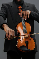 Elegant African American man playing violin in tuxedo on gray background in classical music...