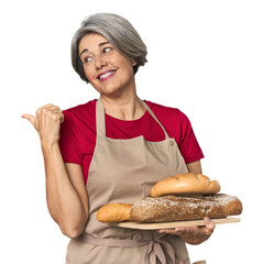 Caucasian mid-age baker with bread loaves points with thumb finger away, laughing and carefree.