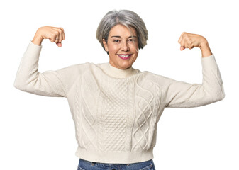 Caucasian mid-age female on studio background showing strength gesture with arms, symbol of...