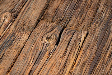 Worn, weathered wooden planks on a wooden pier in Santa Barbara, California (USA). Diagonal old wooden plank surface after long use in different shades of brown. Macro structure with knotholes.