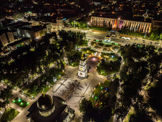 Drone aerial view of a crowd of people at an Easter night service near the cathedral with Chisinau's nightscape in the background, featuring the bell tower, the Triumph Arch, the Government building, 