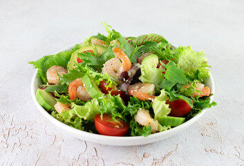 Shrimp salad with avocado, cherry tomatoes, green leaf mix salad and sesame seeds on a white background. 