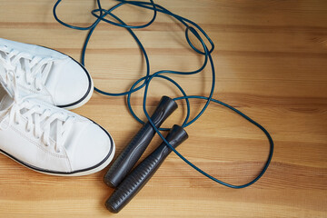 White sneakers and a black jump rope on a wooden parquet, accessories for fitness, home fitness