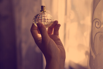 Young female hand holds luxurious faceted bottle with eau de parfum toilet aroma scented water spray.Photo filter in purple colors and tones