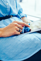 Cropped side view of young woman touching with finger on display of modern tablet choosing audio...
