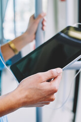 Cropped view of female person holding digital touch pad device with black display and using transport public internet.Young woman with modern tablet in hands standing in tram and listening music