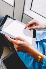Cropped view of young woman choosing audio song in playlist downloaded on modern touch pad with earphones.Female person touching with finger on blank screen area of digital tablet using transport wifi